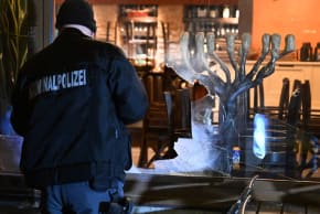 A detective stands with a flashlight in front of the smashed window of an Israeli restaurant in Munich, Germany, April 10, 2026. 