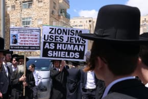 Ultra-Orthodox demonstrators holding a sign reading "Zionism uses Jews as human shields" outside of the IDF's recruitment offices in Jerusalem, April 12, 2026.