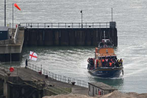 A demonstrator, standing next to an England flag, gestures as a Royal National Lifeboat Institution (RNLI) vessel carrying migrants arrives at the Port of Dover, Britain, April 1, 2026.