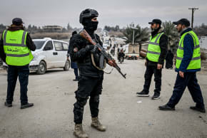 Security forces guard a damaged bridge as people cross over the Euphrates River as Syrian army forces deploy in parts of the eastern province formerly controlled by Kurdish forces following their withdrawal from the area on January 22, 2026 in Deir ez-Zor, Syria. 