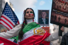 A woman wearing a Lion and Sun Iranian flag (used before the 1980 Islamic Revolution) holds a sign during a protest in solidarity with the anti-government protesters of Iran on February 14, 2026.