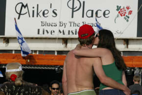 A young Israeli couple kiss 06 May 2003 during a memorial gathering at the beachfront Tel Aviv bar, Mike's Place, which was hit by a suicide bomber a week earlier. The bar reopened as Israelis celebrated their 55th independence day. 