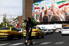 A woman walks past a billboard featuring an image of the late Supreme Leader of Iran, Ayatollah Ali Khamenei, on a building, amid a ceasefire between US and Iran, in Tehran, Iran, April 27, 2026