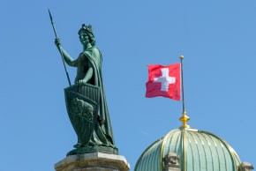 he Helvetia statue in front of a Swiss flag on the Swiss Parliament building (Bundeshaus)