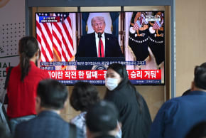People watch a television screen showing a live broadcast of US President Donald Trump delivering national address on war against Iran, at a train station in Seoul on April 2, 2026.