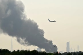 Illustrative; An Emirates aircraft flies past plumes of smoke from an ongoing fire near Dubai International Airport in Dubai on March 16, 2026. (photo credit: AFP VIA GETTY IMAGES)