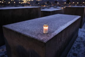 A single lit candle lies on a frost covered concrete block at the Memorial to the Murdered Jews of Europe on January 26, 2026 in Berlin, Germany.