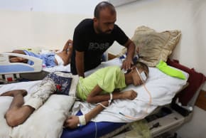 Injured Palestinian Hassan Qlob, 18, who his father says was shot in the head more than two months ago while out seeking food, lies on a bed as he waits for the Rafah crossing to reopen so he can receive treatment abroad, as his father Ibrahim tends to him, after the Israel-Hamas ceasefire.