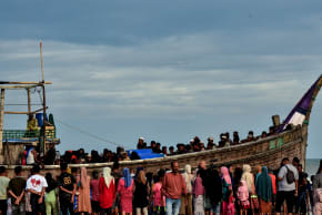 People gather around a boat carrying newly-arrived Rohingya refugees, after authorities prevented the refugees from disembarking and ordered them to remain on board the vessel.