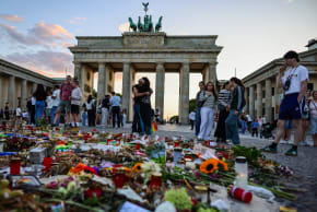 Tourists and visitors observe and pay respects at a makeshift memorial set in Pariser Platz in front of the Brandenburg gate, one week after the Christopher Street Day pride parade attack on August 2, 2026 in Berlin, Germany. 