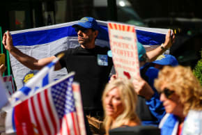 A demonstrator holds an Israeli flag as protesters gather during an '#EndJewHatred' rally outside Poetica Coffee, following a social media post by the shop targeting Jewish Congressman Dan Goldman and denying service to pro‑Israel customers in Brooklyn, New York.