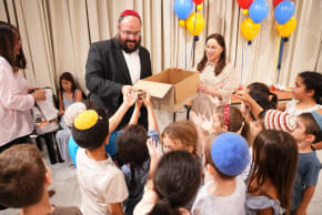 Rabbi Ephraim Duchman, Director of Development of Colel Chabad, distributing gifts to children as Mrs. Rochel Marton looks on.