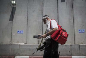 An ultra-Orthodox Jewish man carrying a gun and a first aid bag, walks by the Separation Wall at the entrance to the Jewish religious site of Rachel's Tomb, near Bethlehem, on June 26, 2014.