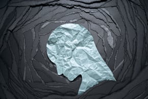 Illustrative image of a head, made of crumpled paper, looking down on a black background. 