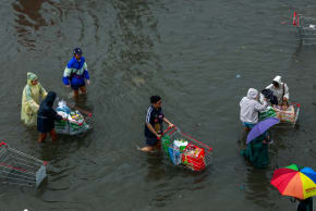 People carry groceries on shopping carts as they wade through a flooded street during heavy rain in Bangkok, Thailand, September 26, 2026.
