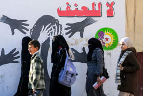 Women walk past a mural with the slogan "no to violence" (against women) drawn on the walls of a school in Syria's northern city of Manbij on December 21, 2024.