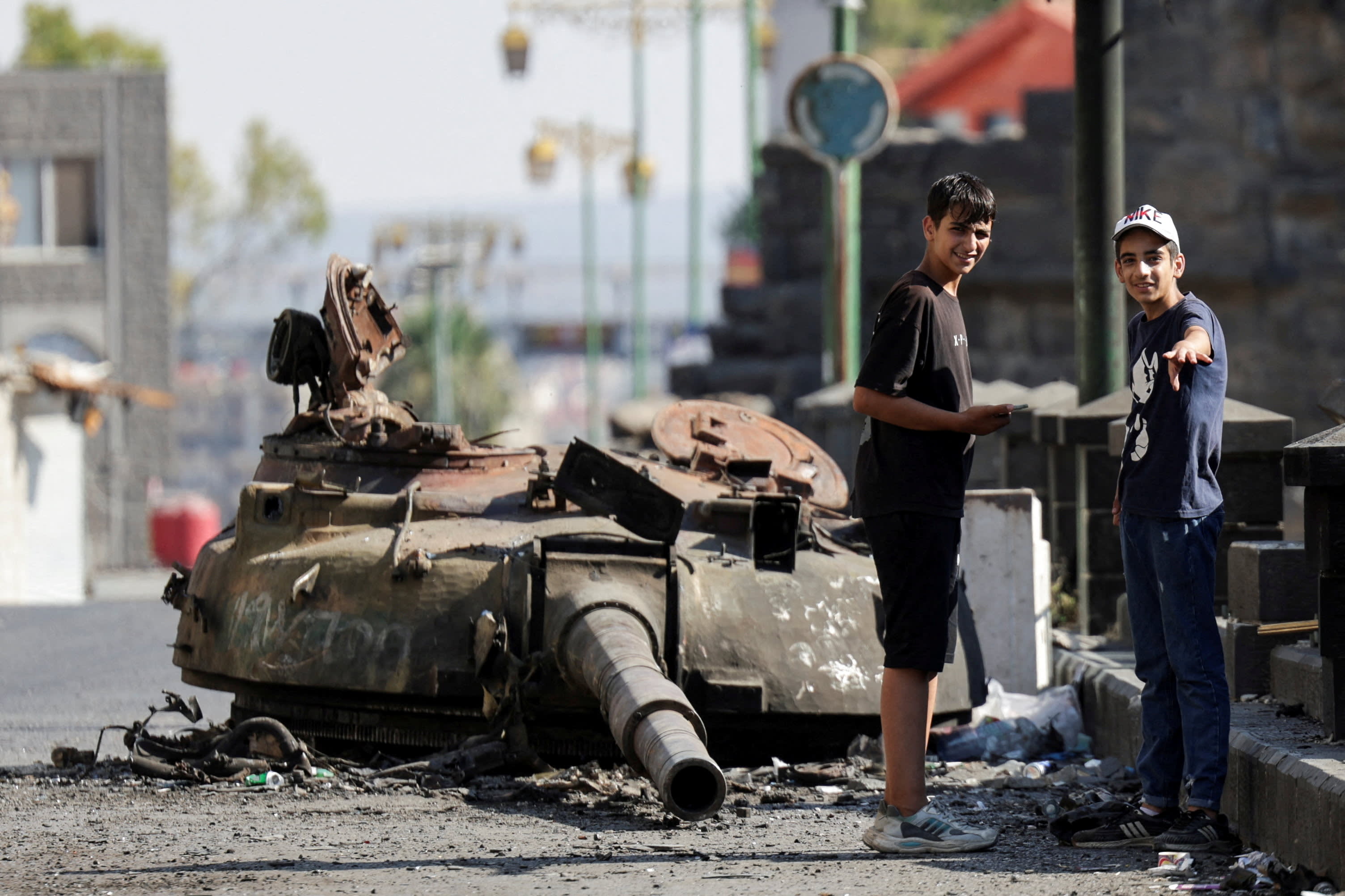 People stand next to a destroyed tank turret, following deadly clashes between Druze fighters, Sunni Bedouin tribes and government forces, in Syria