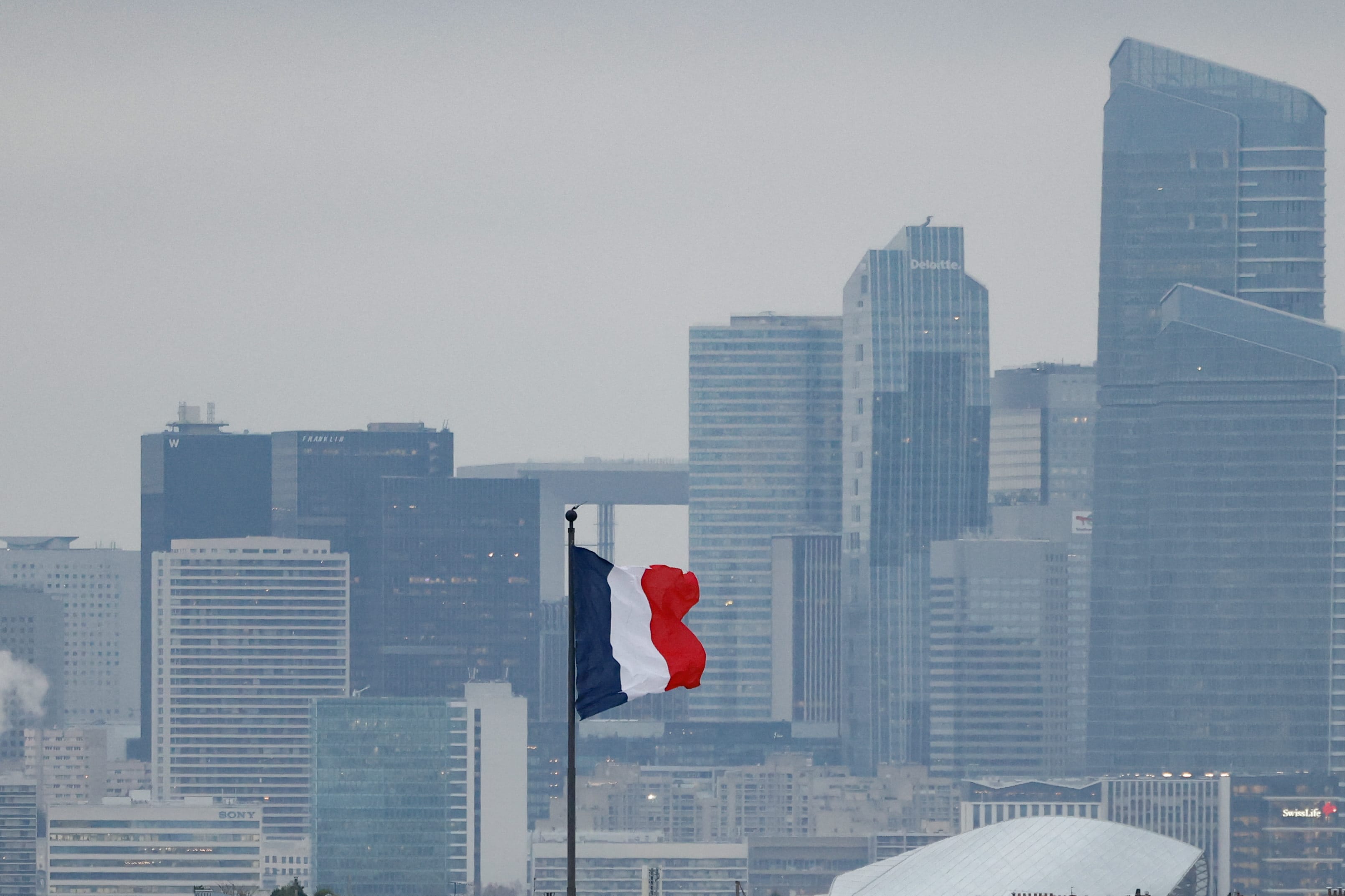 This photograph shows a French flag fluttering with the La Defense business district in the background skyline, in Paris, on December 5, 2025. (photo credit: IAN LANGSDON/AFP via Getty Images)