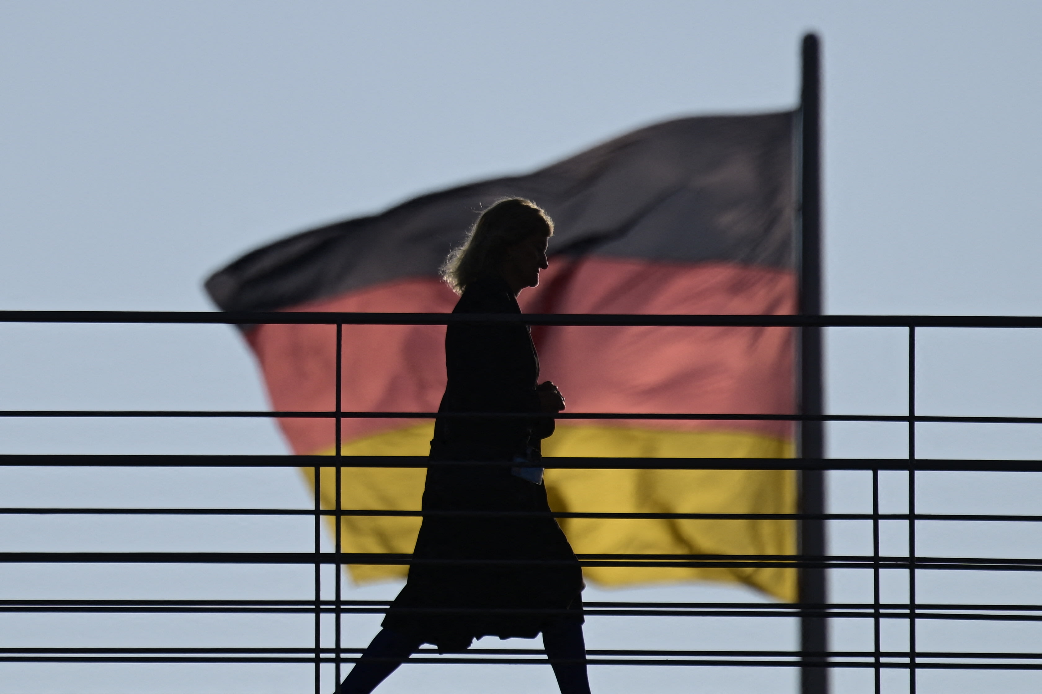 A woman crosses an overpass as in background can be seen one of the German flags flying on the Reichstag building that houses the Bundestag (lower house of parliemant) on November 27, 2025 in Berlin, Germany. (photo credit: John MACDOUGALL / AFP via Getty Images)