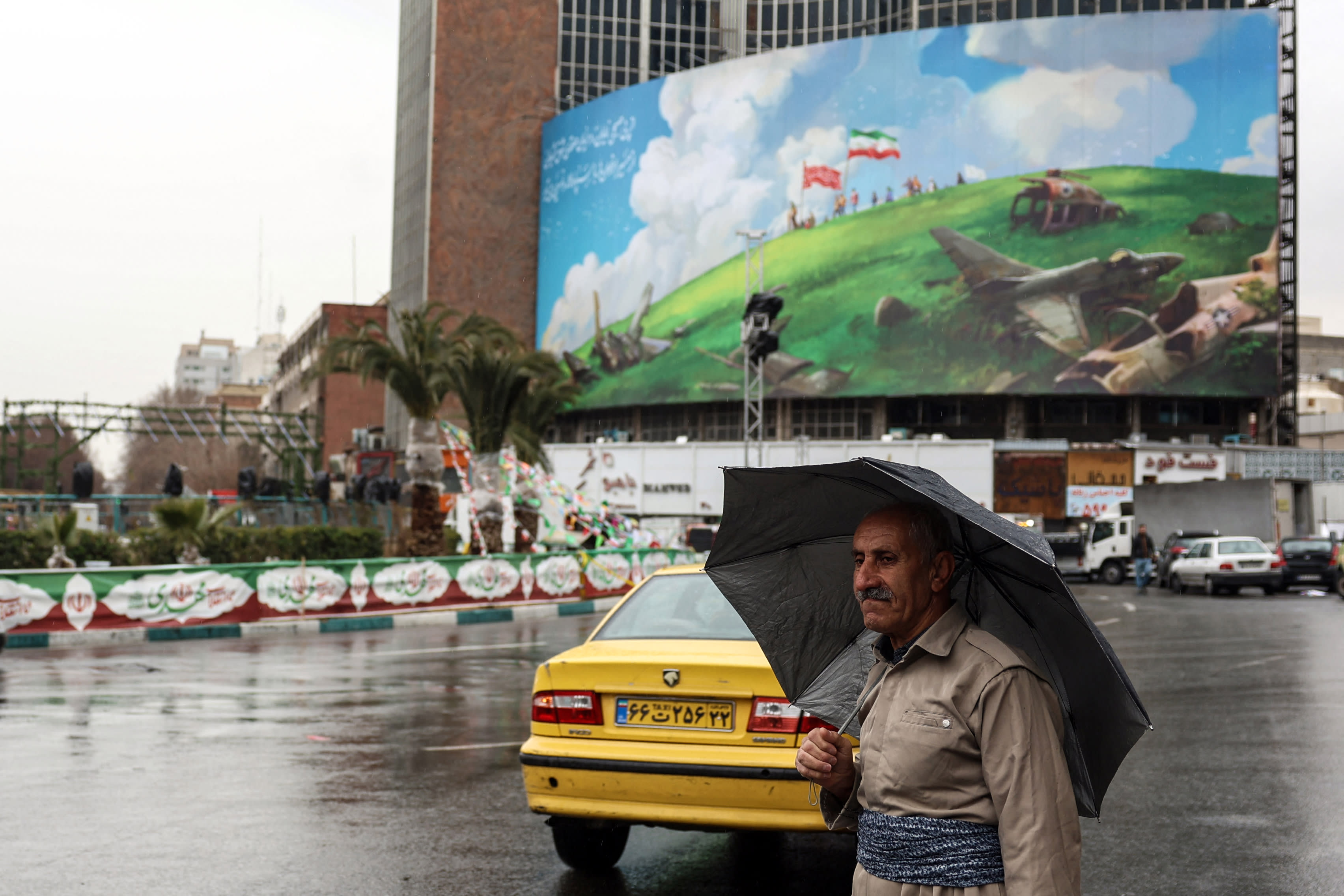 An Iranian Kurdish man in traditional outfit walks past an anti-US billboard displayed on a building in Tehran