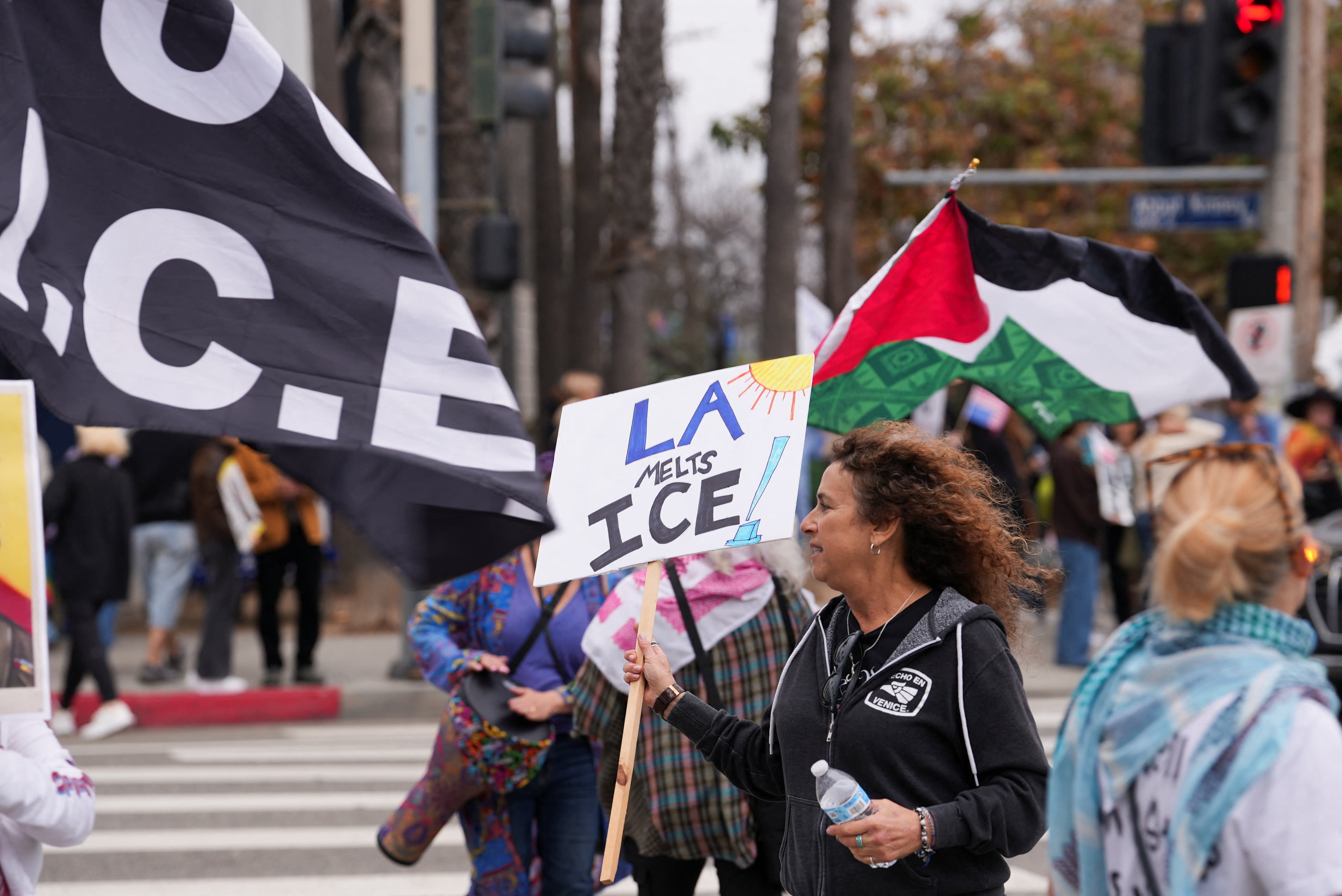 A woman holds a sign reading "LA melts ICE" alongside other demonstrators carrying a Palestinian flag during a protest against U.S. President Donald Trump
