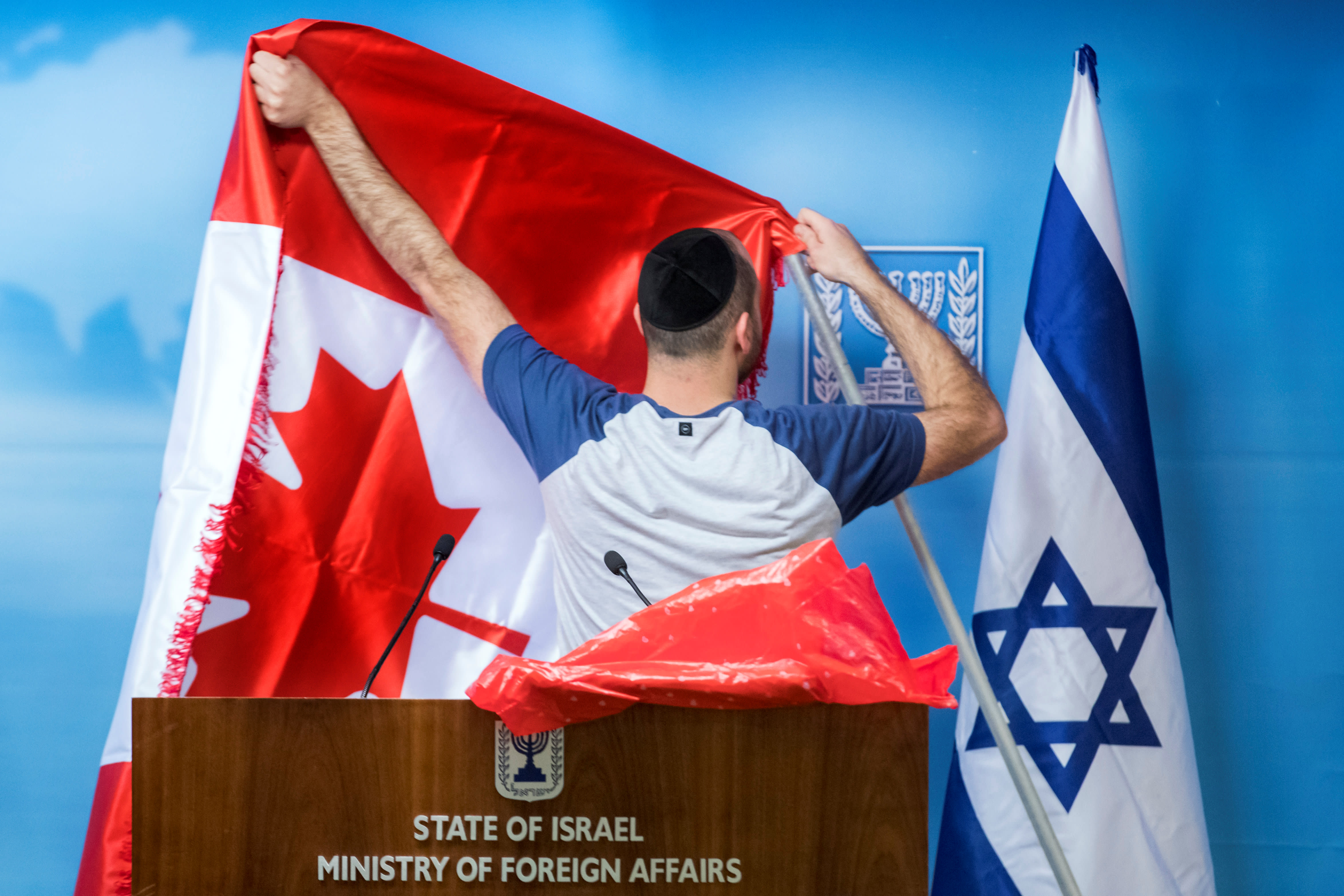 An employee adjusts the Canadian flag next to the Israeli one, at the Foreign Ministry in Jerusalem, October 31, 2018 (photo credit: JIM HOLLANDER/POOL VIA REUTERS)