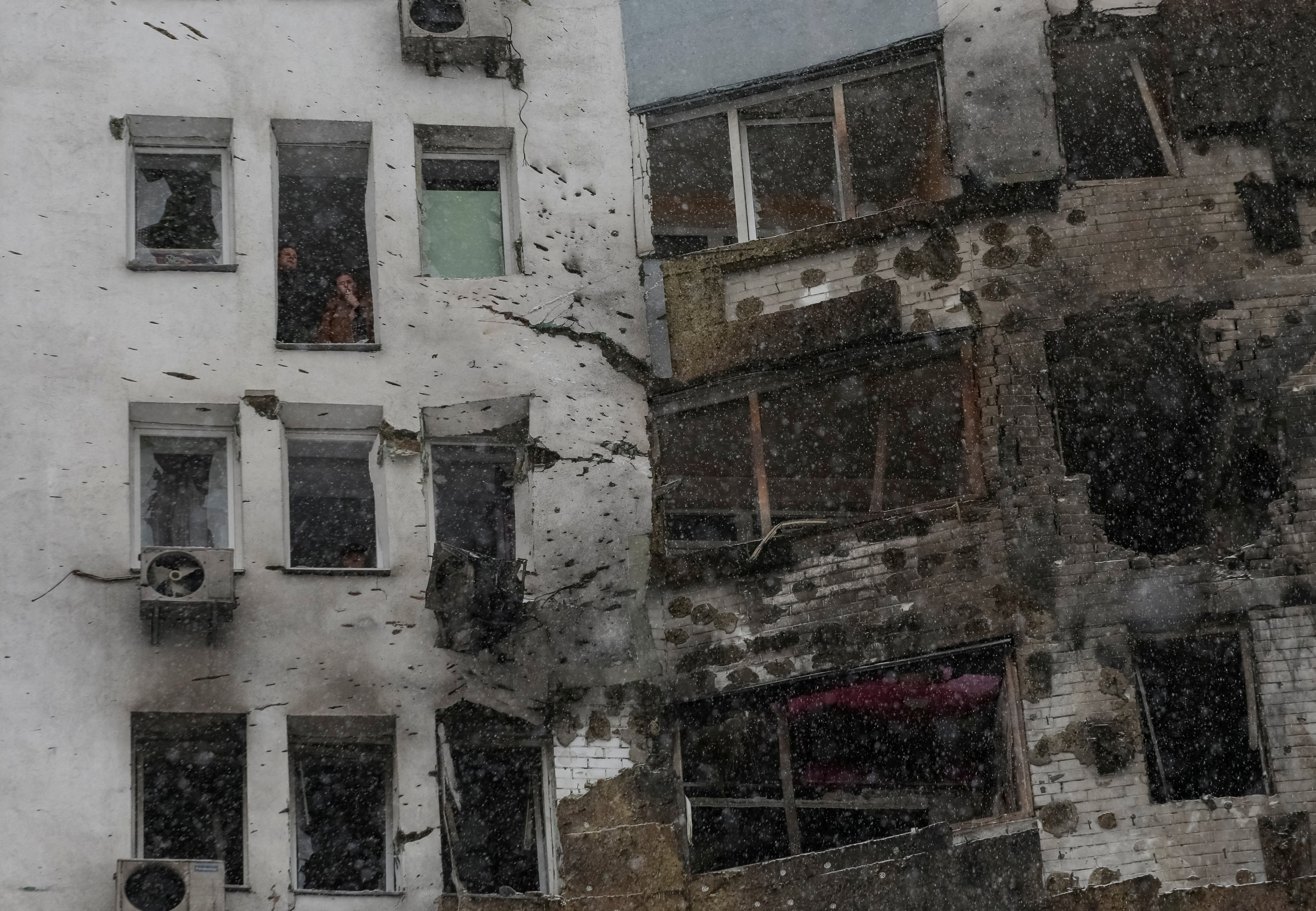 Residents smoke near a broken window of their apartment, damaged during Russian drone strike, amid Russia