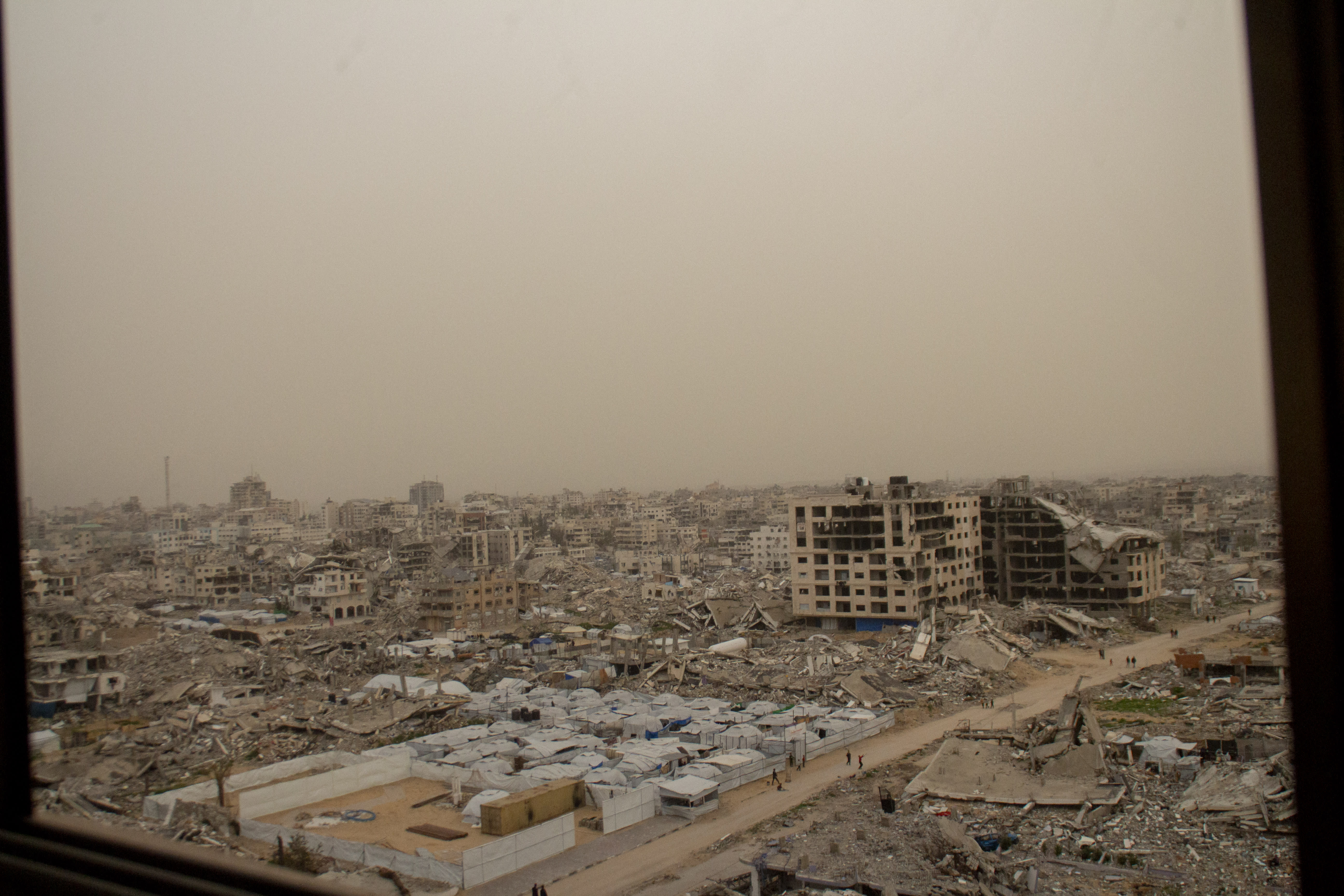 A dust-filled skyline of the Tel al-Hawa neighbourhood in Gaza City is seen through the interior of a damaged building on February 13, 2026; illustrative. (photo credit: Hassan Salem/Middle East Images/AFP via Getty Images)