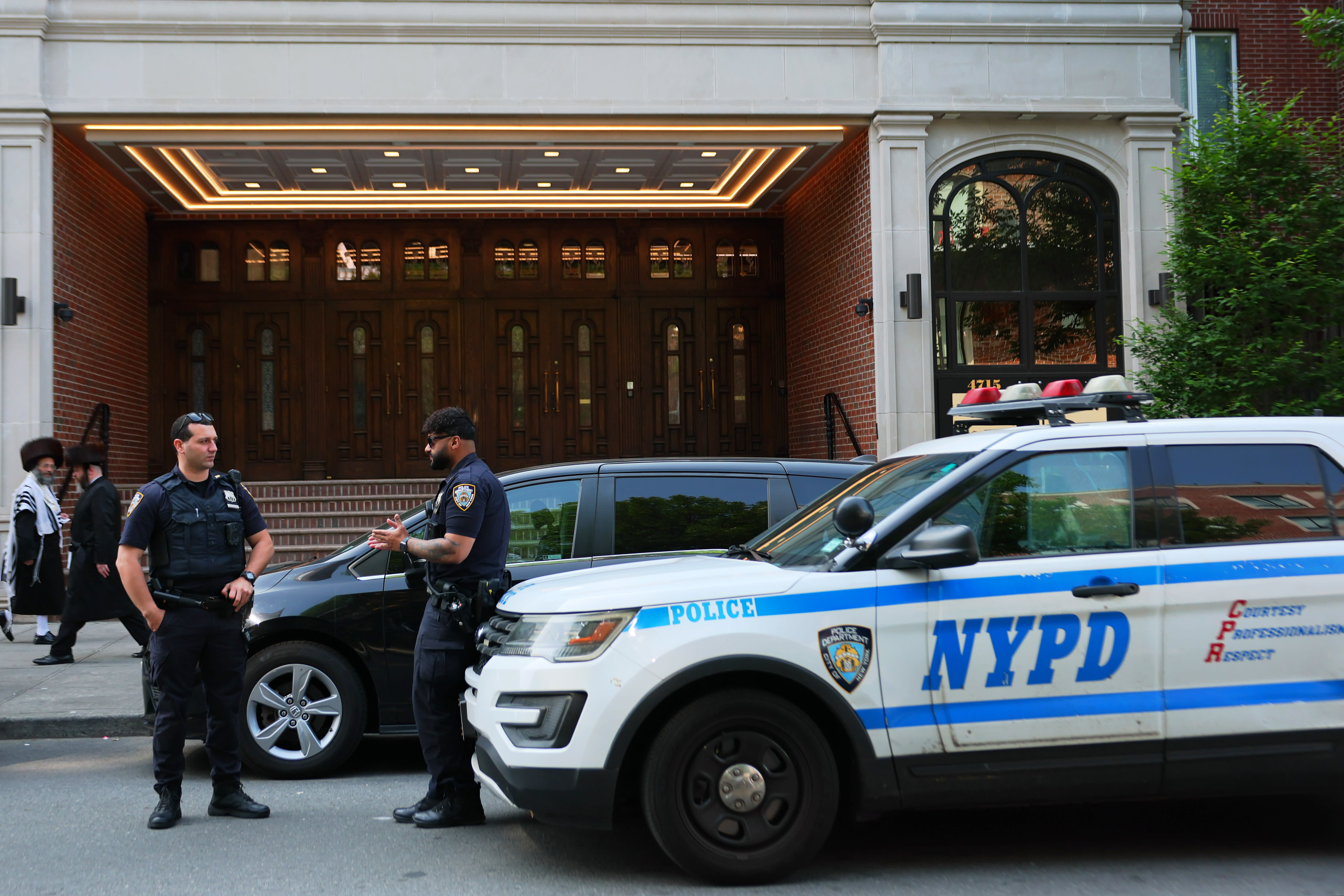 Members of the Orthodox Jewish community walk past NYPD officers as they stand guard outside of Congregation Shaarei Zion of Bobov on June 02, 2025 in the Borough Park neighborhood of the Brooklyn borough in New York City (Illustrative).   (photo credit: MICHAEL M. SANTIAGO/GETTY IMAGES)