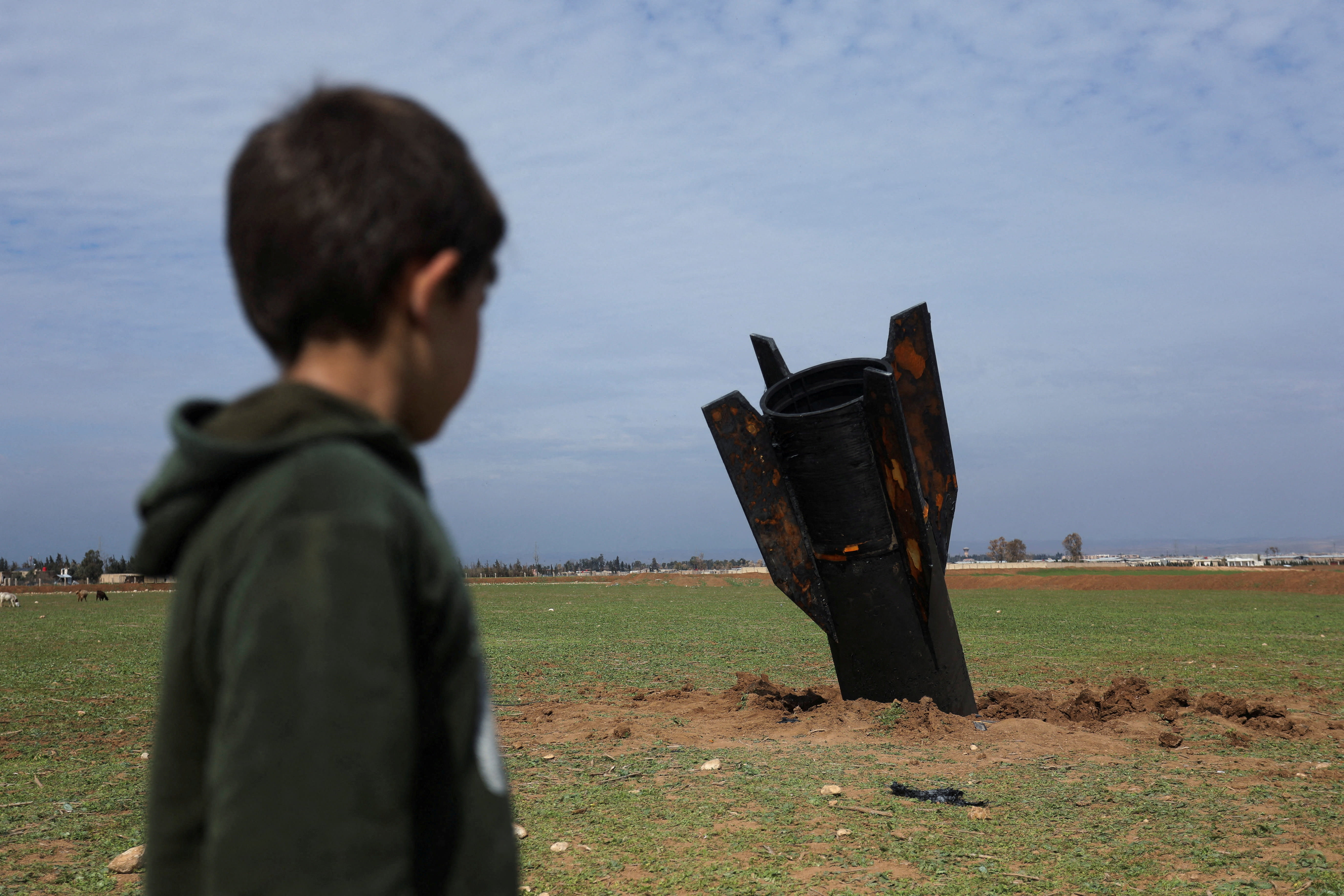 A child stands next to a missile after it fell near Qamishli International Airport, amid the US-Israeli conflict with Iran, in Qamishli, Syria, March 4, 2026. (photo credit: REUTERS/Orhan Qereman)