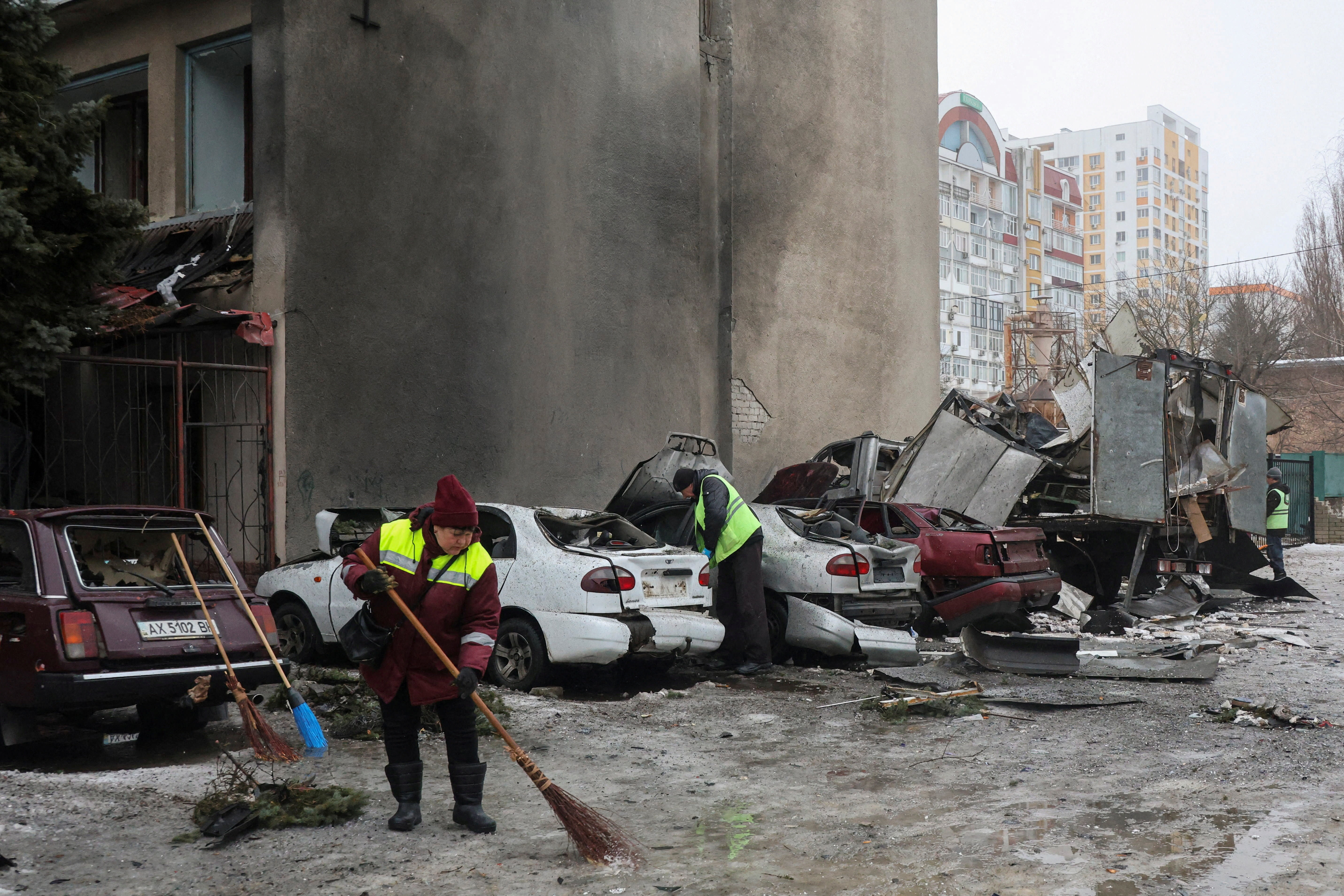 Municipal workers remove debris next to damaged cars outside an apartment building hit by a Russian drone strike on Thursday, amid Russia