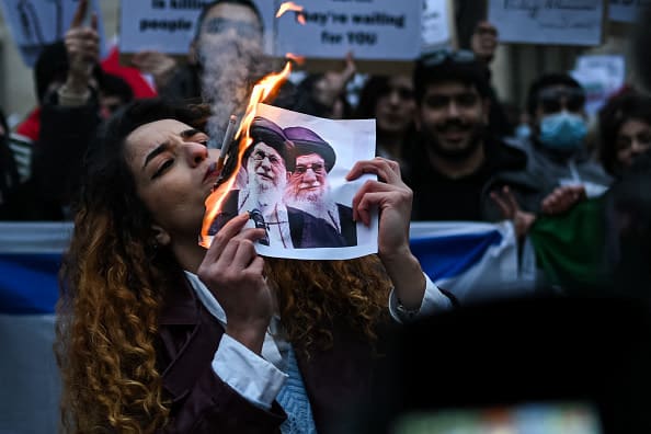 An anti-Iranian regime protester lights a cigarette with a lit paper depicting Ali Khamenei, Supreme Leader of Iran during a gathering outside the US Consulate in Milan, on January 13, 2026. (photo credit: Piero CRUCIATTI / AFP via Getty Images)