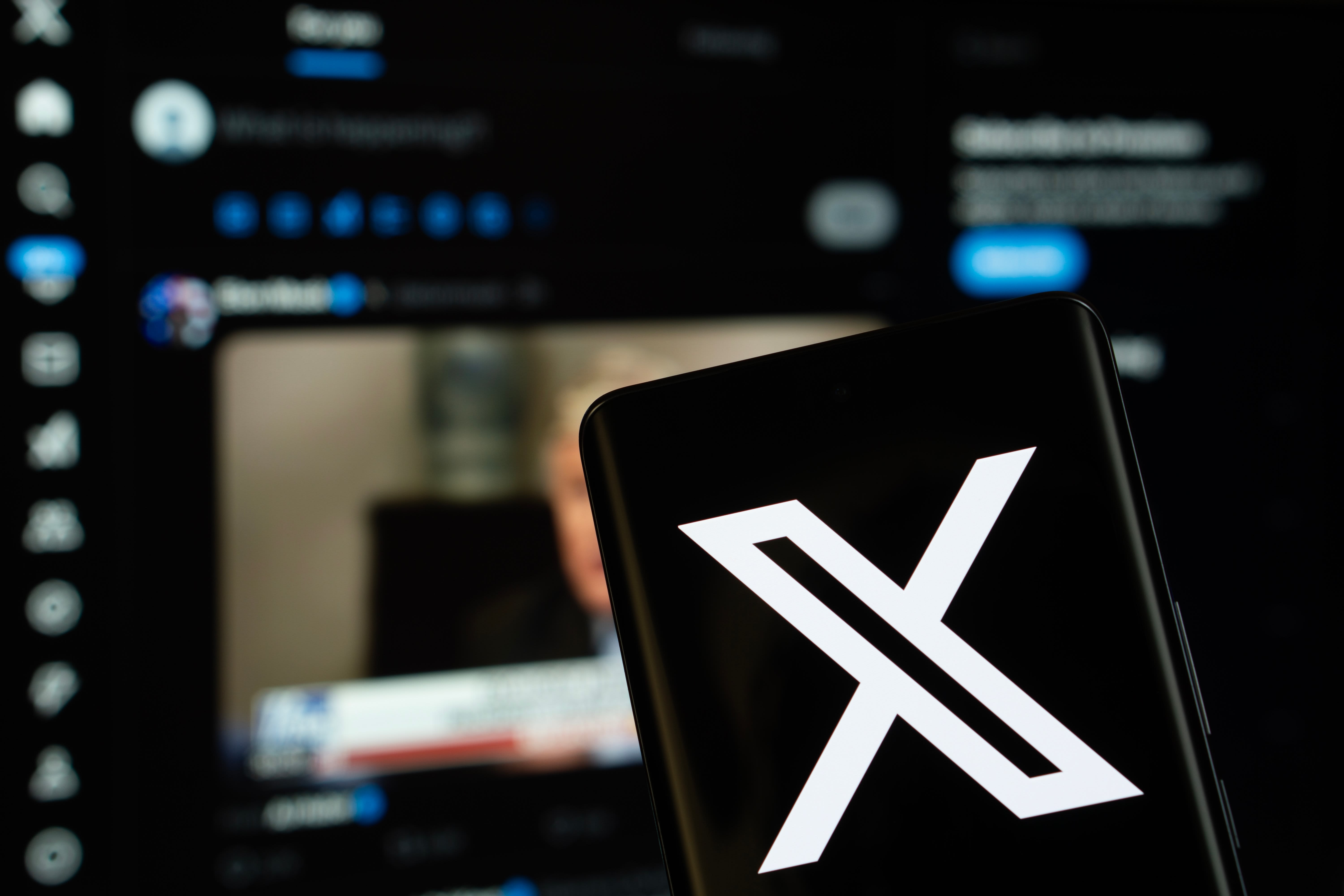 X (twitter) logo is seen on a smartphone, with the bluesky website visible on a computer screen in the background. (photo credit: Bangla press/Shutterstock)