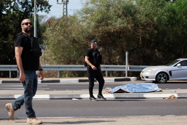  Israeli security personnel walk near the body of a dead man, as Hamas launches a surprise attack from the Gaza Strip, near Ashkelon, southern Israel October 7, 2023.  (photo credit: REUTERS/AMMAR AWAD)