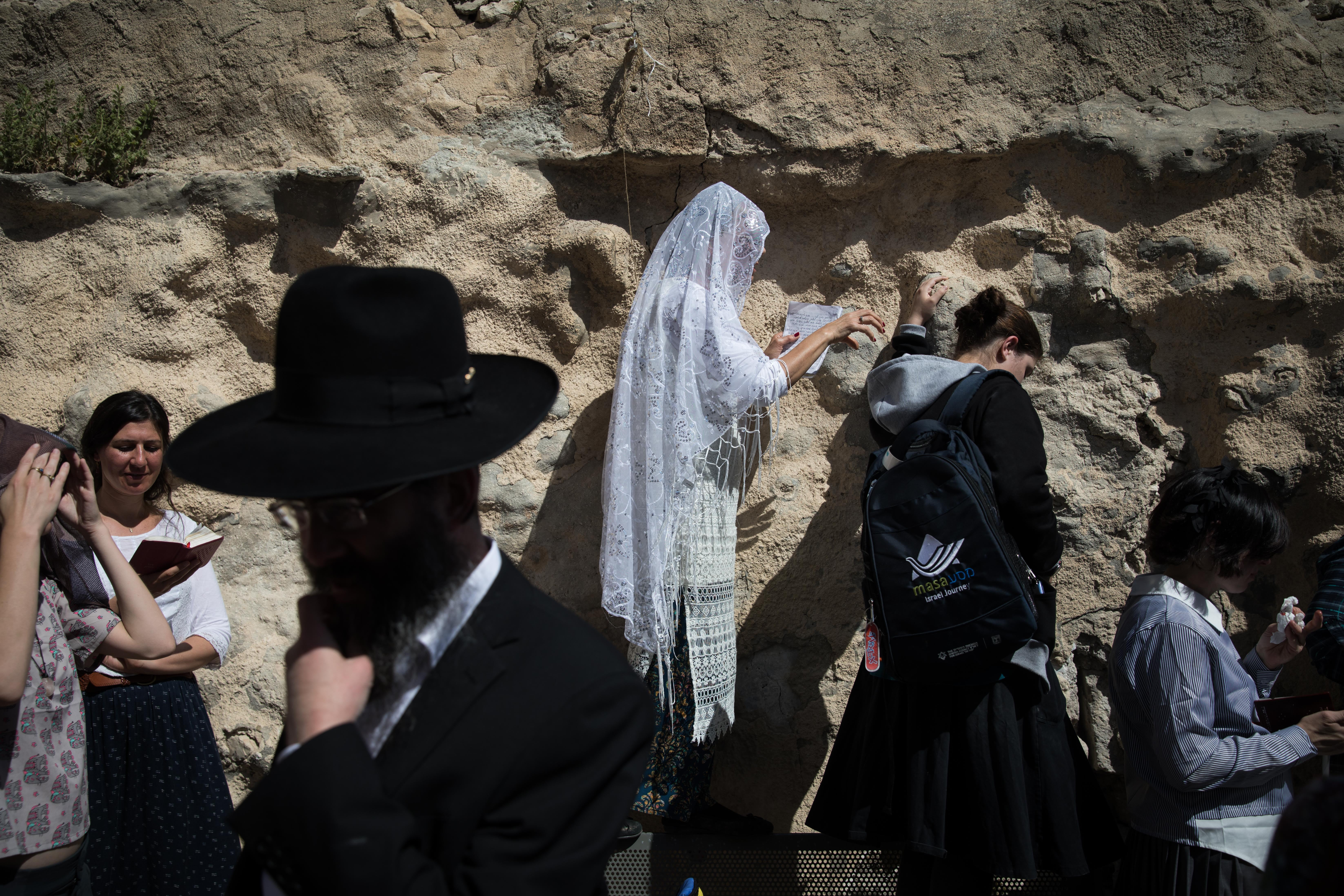 A Jewish woman covered in a white prayer shawl prays in front of the Western Wall in Jerusalem