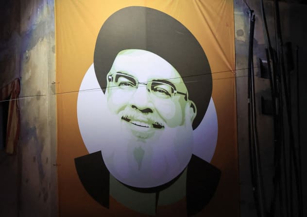 An image of the group's late leader Hassan Nasrallah hangs from a building as people watch atop near the site where Nasrallah was killed, before the first anniversary of his assassination in an airstrike, in Beirut's southern suburbs, Lebanon, September 26, 2025.