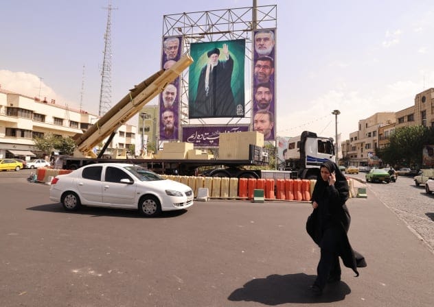 A woman walks past a deactivated Kheibar Shekan ballistic missile in front of a picture of Iran's Supreme Leader Ayatollah Ali Khamenei in Tehran's Bahrestan Square on September 27, 2025, as part of an exhibit to mark the "Sacred Defense Week" commemorating the 1980-88 Iran-Iraq war.