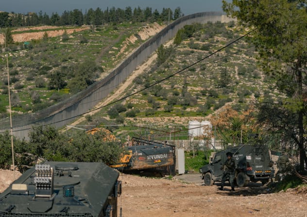 Israeli military vehicles move along a road next to a concrete barrier close to the village of Beit Awwa near Hebron in the West Bank