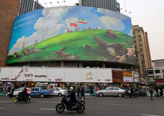 An Iranian rides a moped past a huge anti-US billboard displayed on a building in Tehran's Valiasr Square on February 8, 2026.