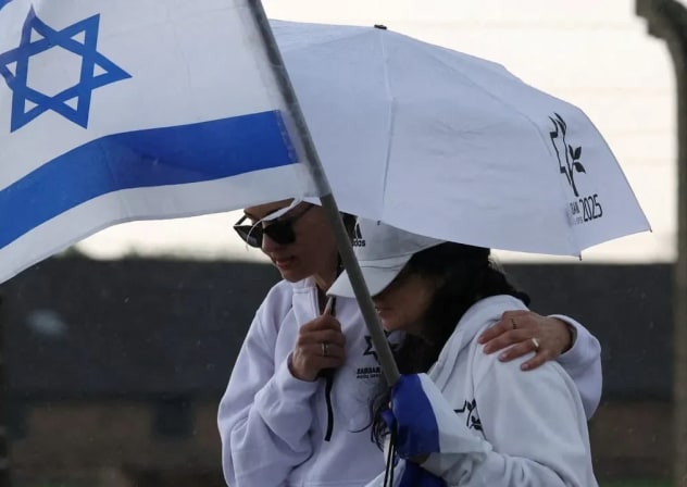 Una mujer sostiene una bandera israelí y otra persona la protege de la lluvia durante la Marcha de los Vivos en Auschwitz-Birkenau en abril. Nacidos en el pacto posterior a Auschwitz, considerábamos que el odio hacia los judíos era algo pasado, condenado al fracaso, como el racismo