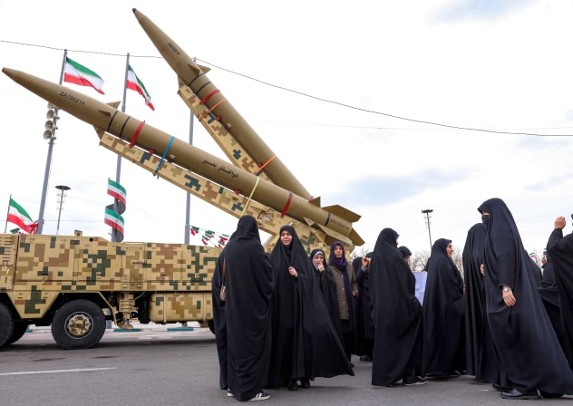 Women walk near ballistic missile launch vehicles in Tehran on February 11, 2026, during a rally marking the 47th anniversary of the 1979 Islamic revolution. 