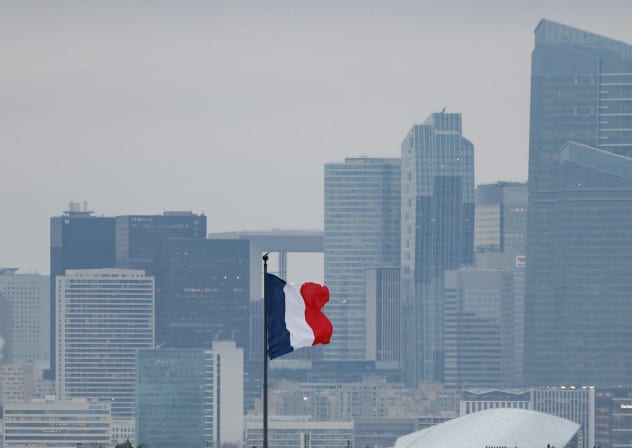This photograph shows a French flag fluttering with the La Defense business district in the background skyline, in Paris, on December 5, 2025.