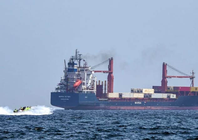 Una embarcación se aproxima al buque portacontenedores Marsa Victory, con bandera de San Cristóbal y Nieves, mientras navega por las aguas del estrecho de Ormuz, frente a la costa de Khasab, en la península de Musandam, al norte de Omán, el 25 de junio de 2025. 
