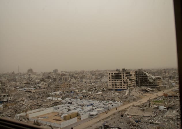 A dust-filled skyline of the Tel al-Hawa neighbourhood in Gaza City is seen through the interior of a damaged building on February 13, 2026; illustrative.