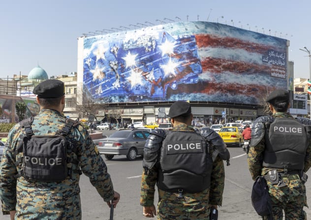 Iranian riot police stand in front of anti-US billboard depicting destruction of aircraft carrier, in Tehran, February 21, 2026; illustrative.