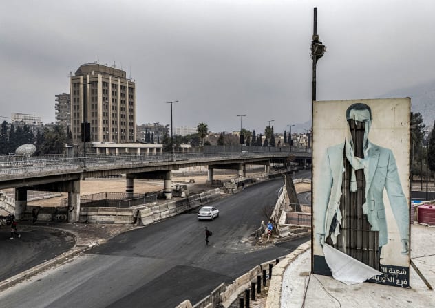 This aerial view shows a man crossing a road near defaced billboard atop a building depicting Syria's ousted president Bashar al-Assad in Damascus on December 24, 2024.