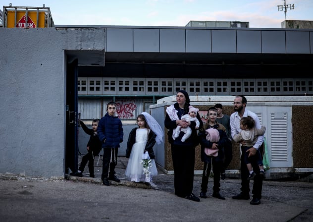 An ultra-Orthodox Jewish family stands outside a bomb shelter after hearing an alert that Iranian missiles are on their way, after Iran launched missile barrages following attacks by the US and Israel on Saturday, in Haifa, northern Israel March 1, 2026.The wedding dress is a costume.