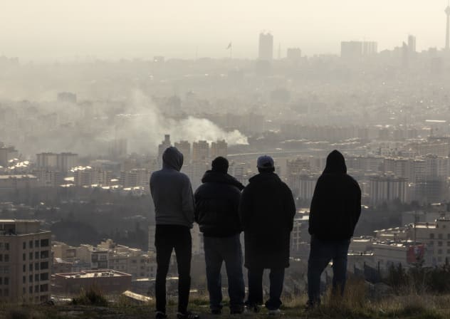 Men watch from a hillside as a plume of smoke rises after an explosion on March 2, 2026 in Tehran, Iran.