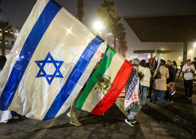 A man draped in a US flag holds stacked Israeli and Royal Iranian flags during a demonstration in solidarity with the Iranian protest movement outside the US Embassy branch office in Tel Aviv on February 14, 2026. 