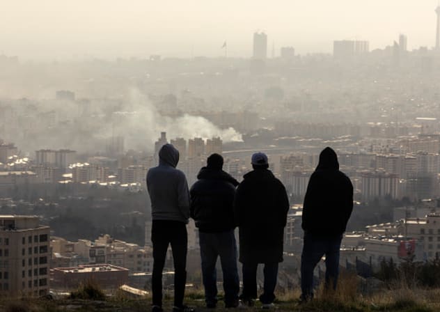 Men watch from a hillside as a plume of smoke rises after an explosion on March 2, 2026 in Tehran, Iran. 